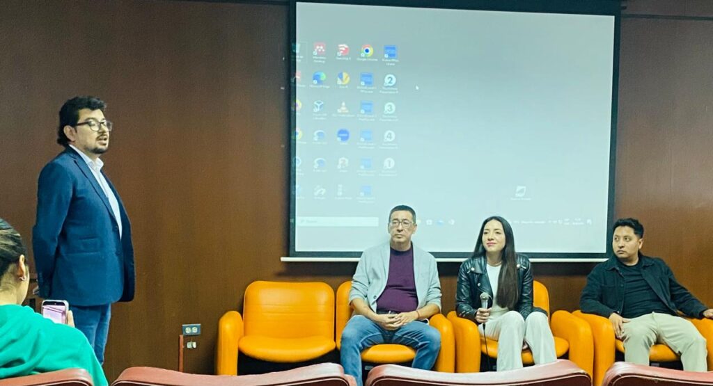 Panel de conferencia en la Pontificia Universidad Católica del Ecuador sobre #NosFaltan3, con varios expositores sentados frente a una pantalla de proyección mientras una persona interviene de pie.
